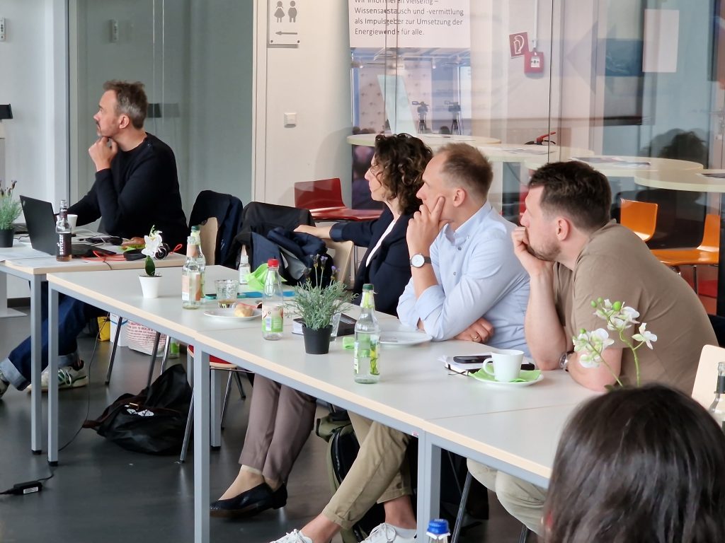 Teilnehmende der Workshopveranstaltung in Nürnberg sitzen an einer Tischreihe und hören den Vortragenden zu